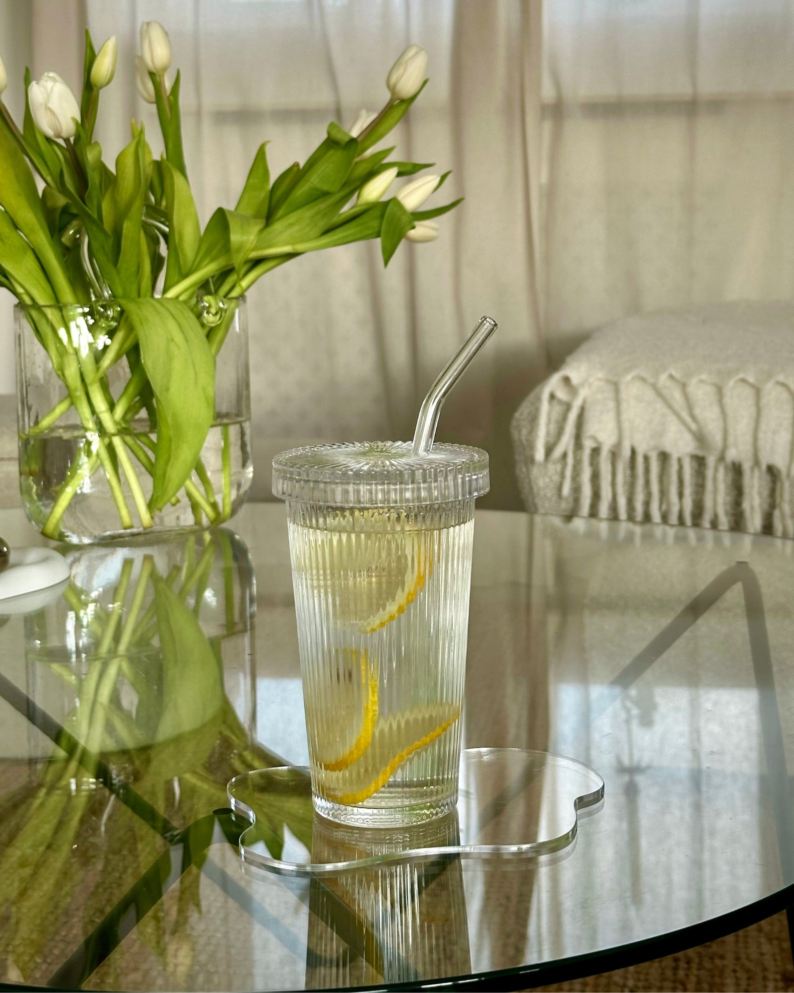 Citronvand serveret i Emily riflet to go drikkeglas i glasdesign med glassugerør på Isabella Akryl drinkunderlag og bordskåner samt Lily håndtaskevase med hvide roser til pynt